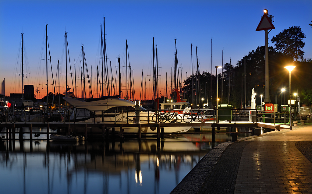 Neustadt in Holstein. Segelboote und Yachten am Anleger. Unterer Jungfernstieg an der Neustädter Bucht nach Sonnenuntergang. Uferpromenade